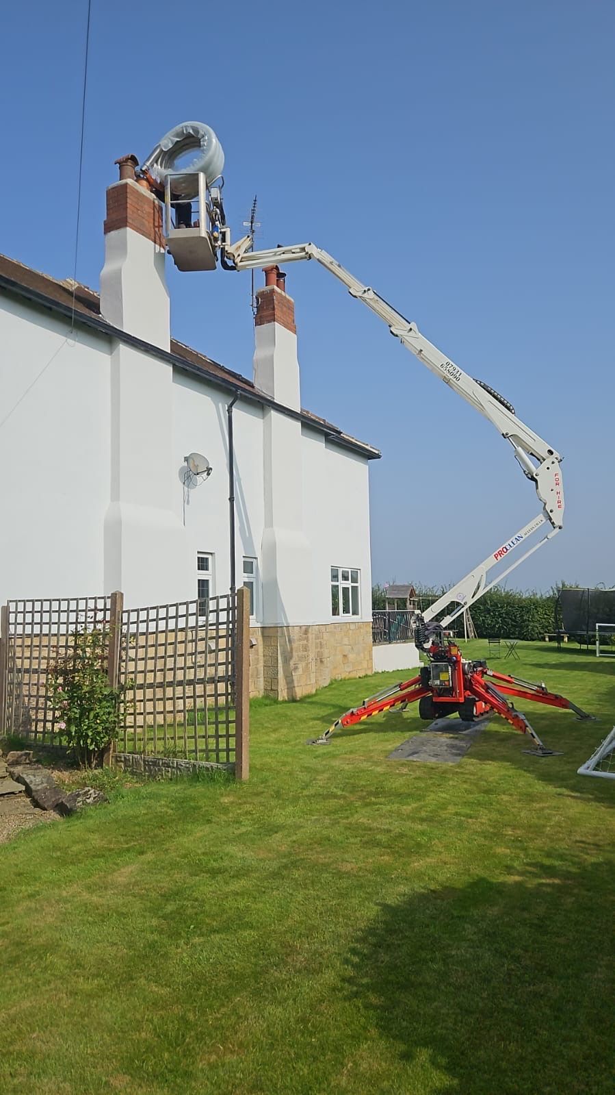 Cherry picker at chimney of white rendered cottage, blue summer sky