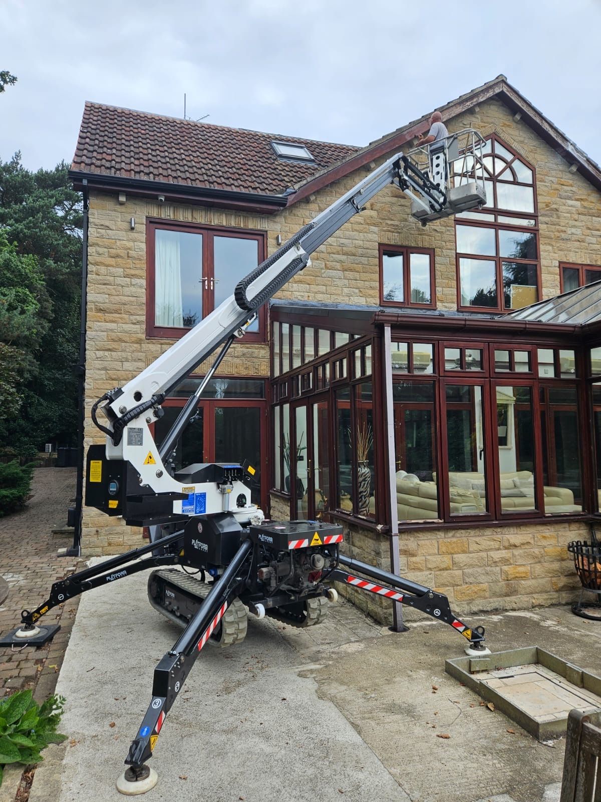 Spider tracked platform on domestic patio, operator in basket at roofline