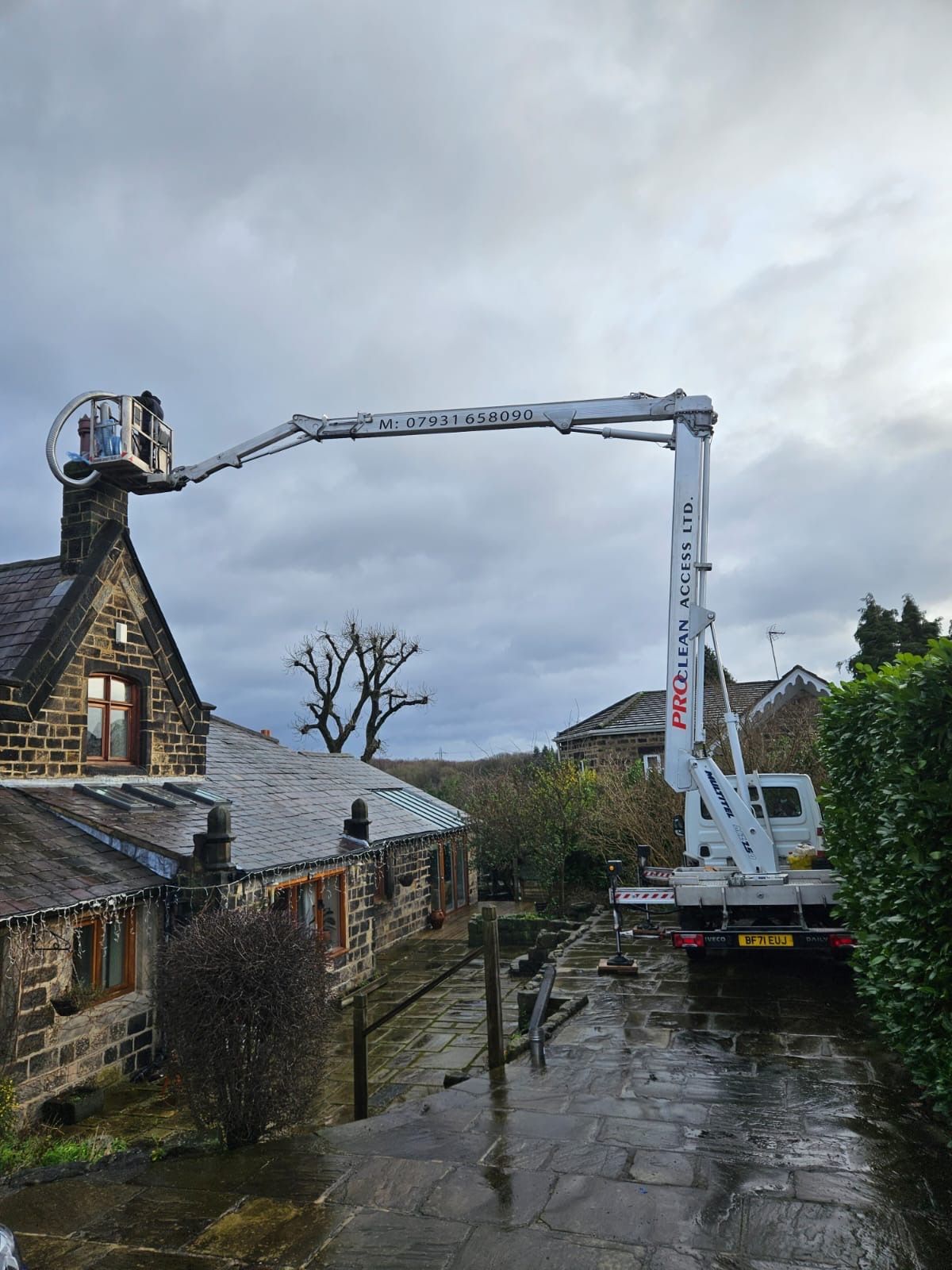 Truck-mounted cherry picker at stone cottage, operator working on chimney stack